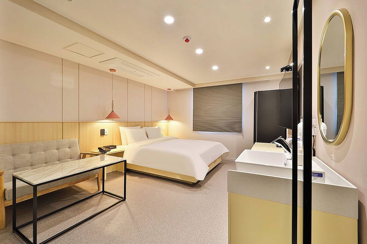 Ein Hotelzimmer mit Bett, einer Couch, einem Schreibtisch, einem Spiegel und einem Badezimmer mit Waschbecken und Spiegel.