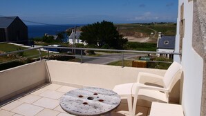 Un balcón con una mesa redonda y dos sillas, con vista a un paisaje costero con casas y el mar.