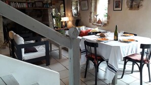 Un comedor con una mesa preparada para dos personas, sillas, una escalera y una estantería al fondo.