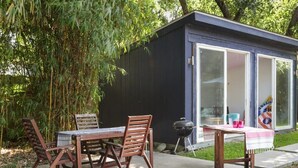 A small, dark blue shed with a sliding glass door, a table with chairs, and a barbecue grill outside.