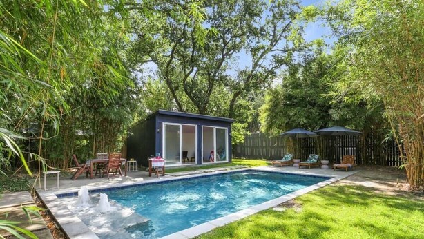A backyard with a swimming pool, a small covered seating area, and a fenced garden.