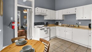 A compact kitchen with white cabinets, a stove, and a dining table with chairs.