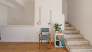 Eine Treppe mit Holzstufen, ein Sessel mit blauer Sitzkissen sowie ein kleines Regal mit Pflanze und Büchern.