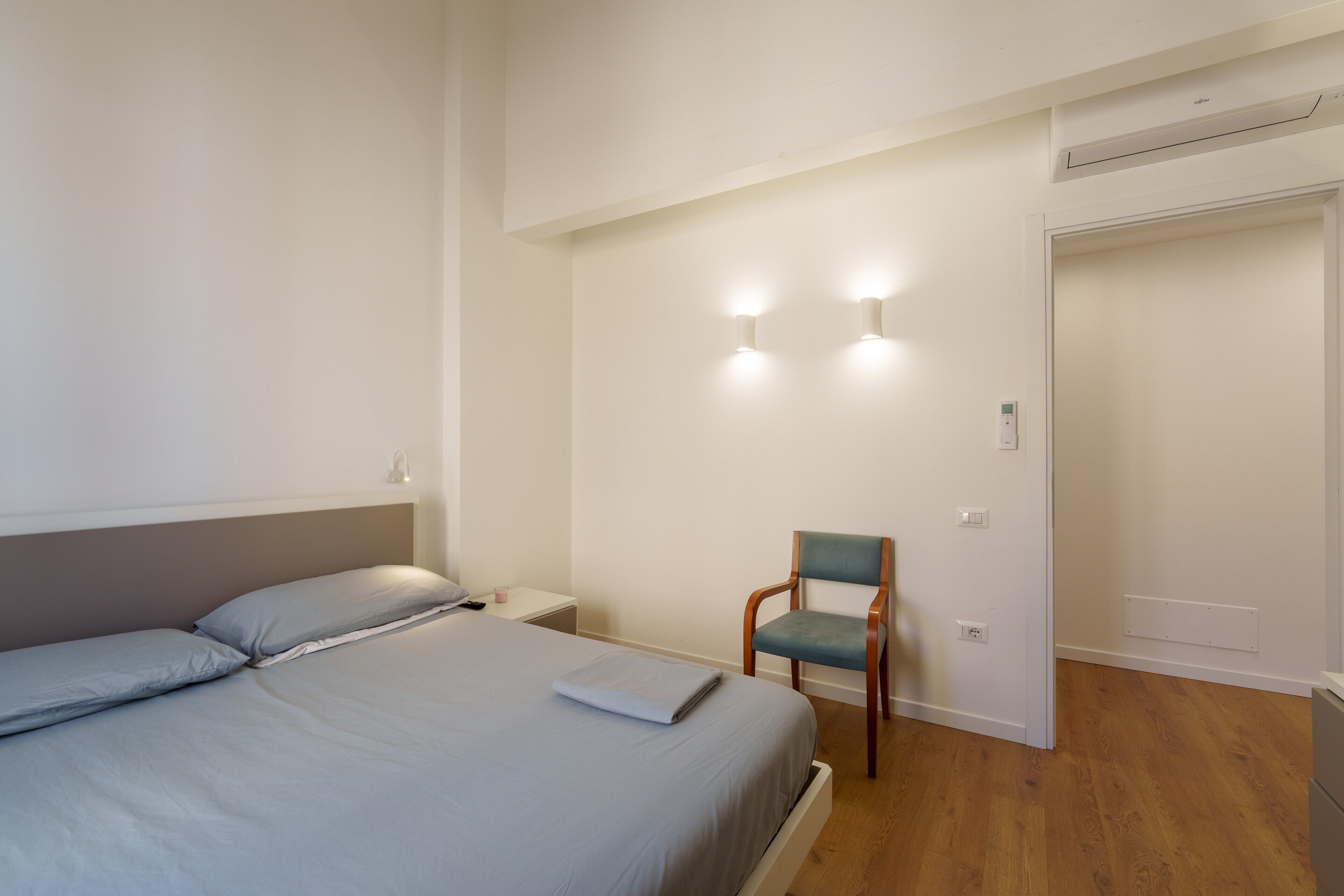 Une chambre à coucher comprenant un lit, une chaise, une table de chevet et un luminaire fixé au mur.
