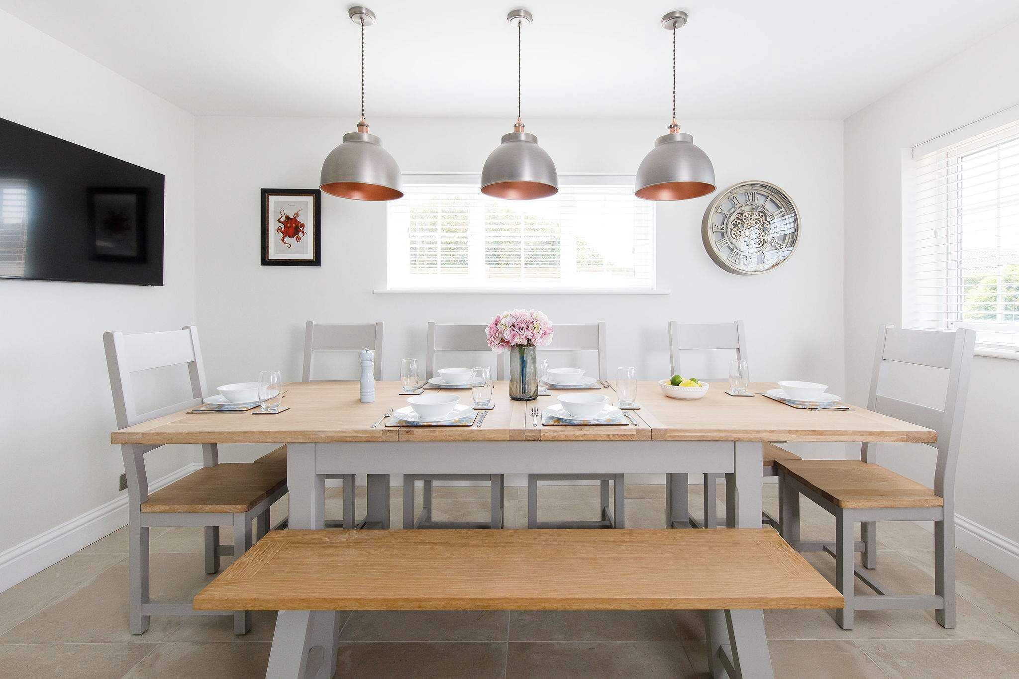 A dining area with a wooden table set for six, white chairs, and three pendant lights.