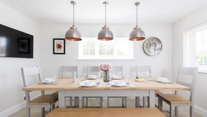A dining area with a wooden table set for six, white chairs, and three pendant lights.