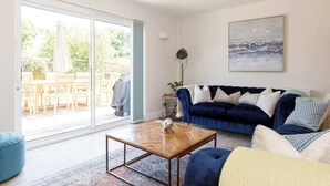 A living room with a dark blue sofa, a wooden coffee table, and a large window with a view of an outdoor patio.