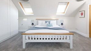 A bedroom with a white bed, two bedside tables, a skylight, and a framed picture on the wall.
