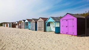Une rangée de cabanes de plage aux toits de couleurs et de styles différents, alignées sur une plage de sable.