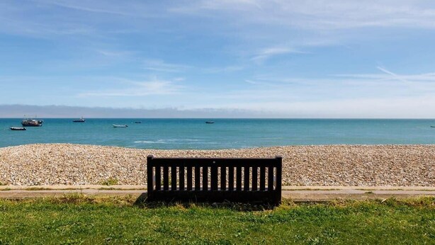A bench by a pebble beach with the sea and boats in the background. - Wonderful Seafront Home - Panoramic Ocean Views (Selsey)