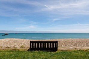 A bench by a pebble beach with the sea and boats in the background. - Wonderful Seafront Home - Panoramic Ocean Views (Selsey)