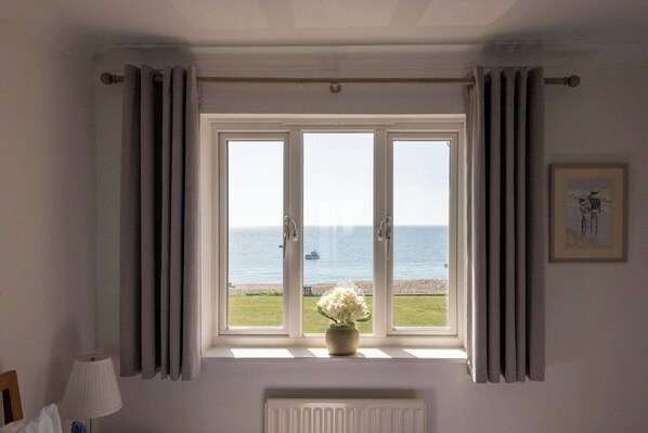 A room with a large window overlooking a body of water, a radiator below the window, and a lamp to the left. - Wonderful Seafront Home - Panoramic Ocean Views (Selsey)