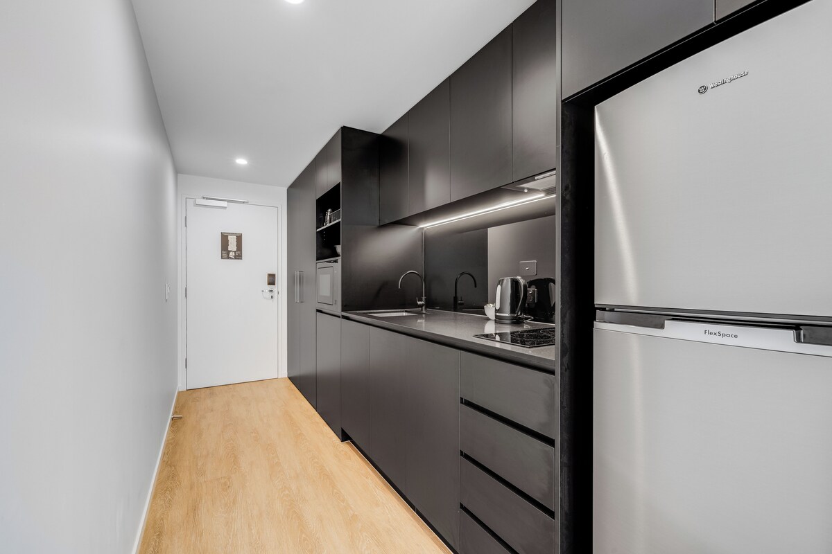 Une cuisine moderne avec des meubles noirs, un réfrigérateur en acier inoxydable et un plancher en bois.