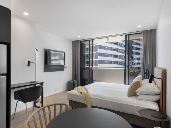 Une chambre d’hôtel moderne équipée d’un lit, d’un bureau, d’une chaise, d’une télévision et offrant une vue sur un immeuble grâce à de grandes fenêtres.