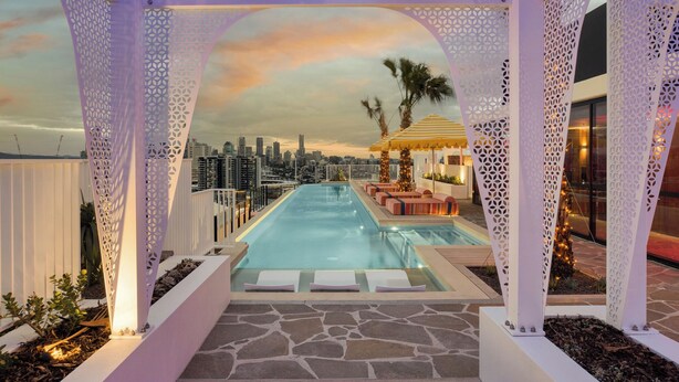 Piscina en la azotea con vistas a la ciudad, zona de estar con sombrillas y paneles de celosía blanca decorativa.