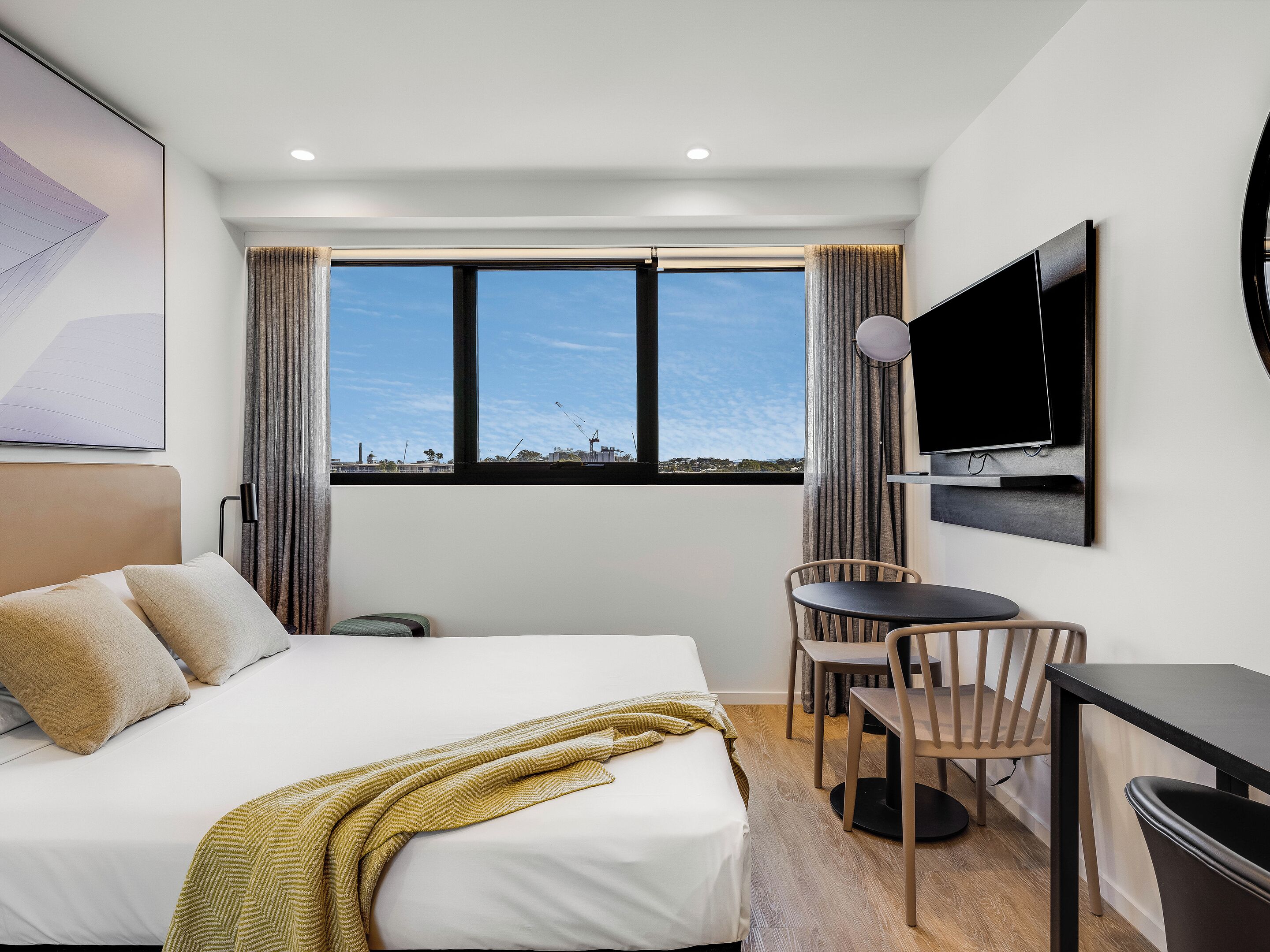 A hotel room with a bed, a desk, a chair, a television, and a large window with a view of the city.