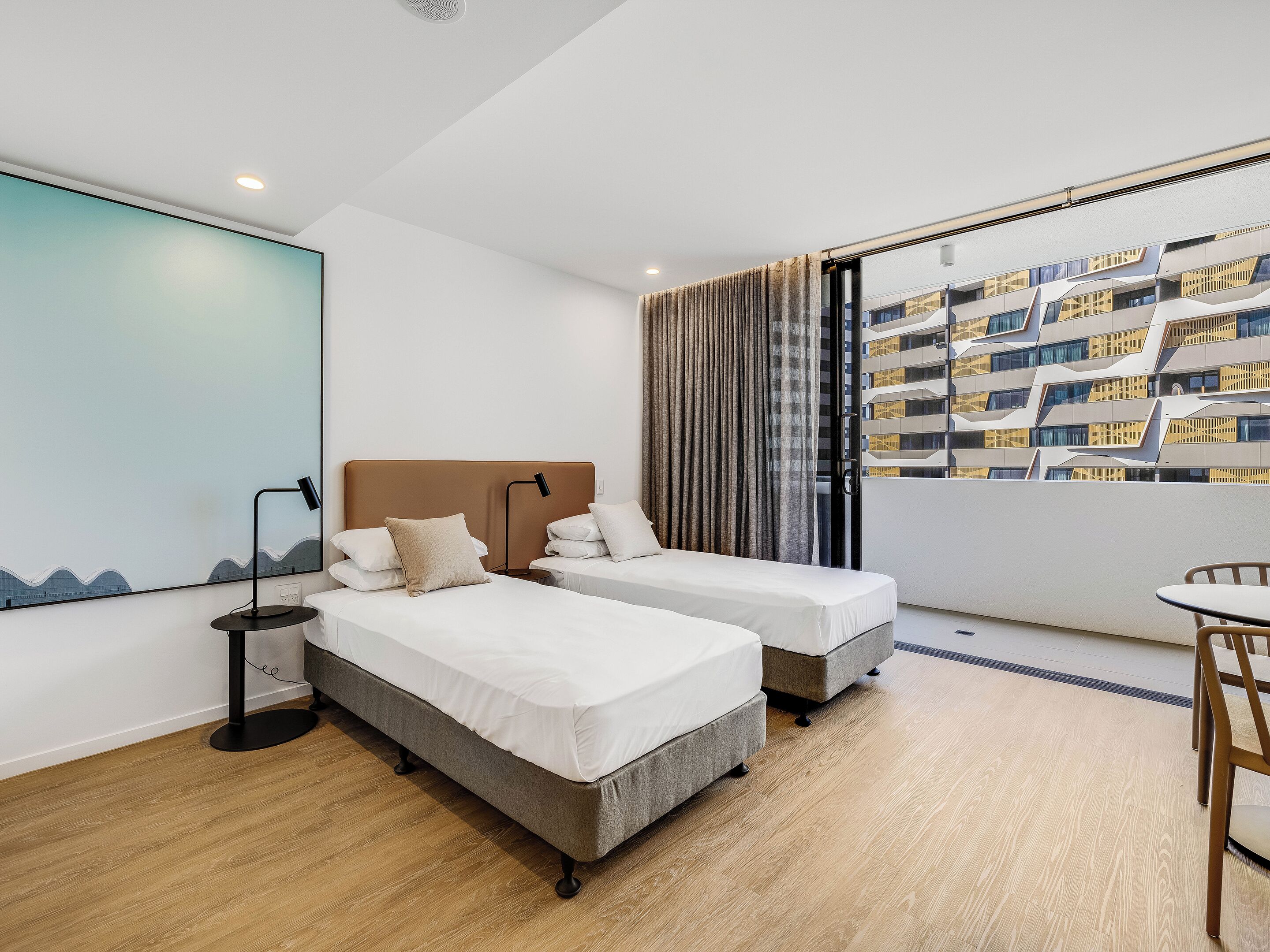 A hotel room with two beds, a desk, and a view of a modern building.