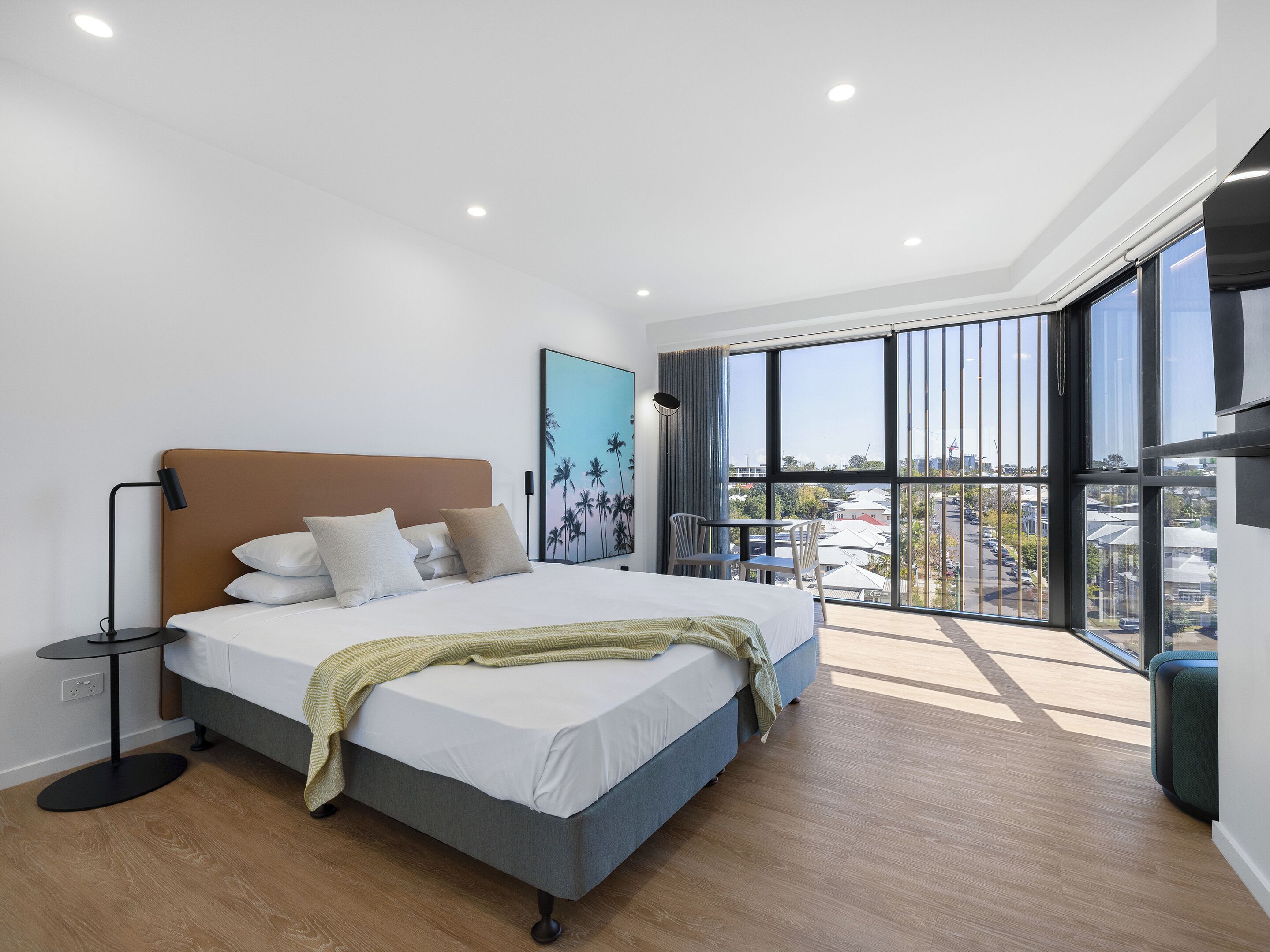 Ein modernes Schlafzimmer mit einem großen Bett, einem kleinen Tisch und einem Balkon mit Blick auf die Stadt.