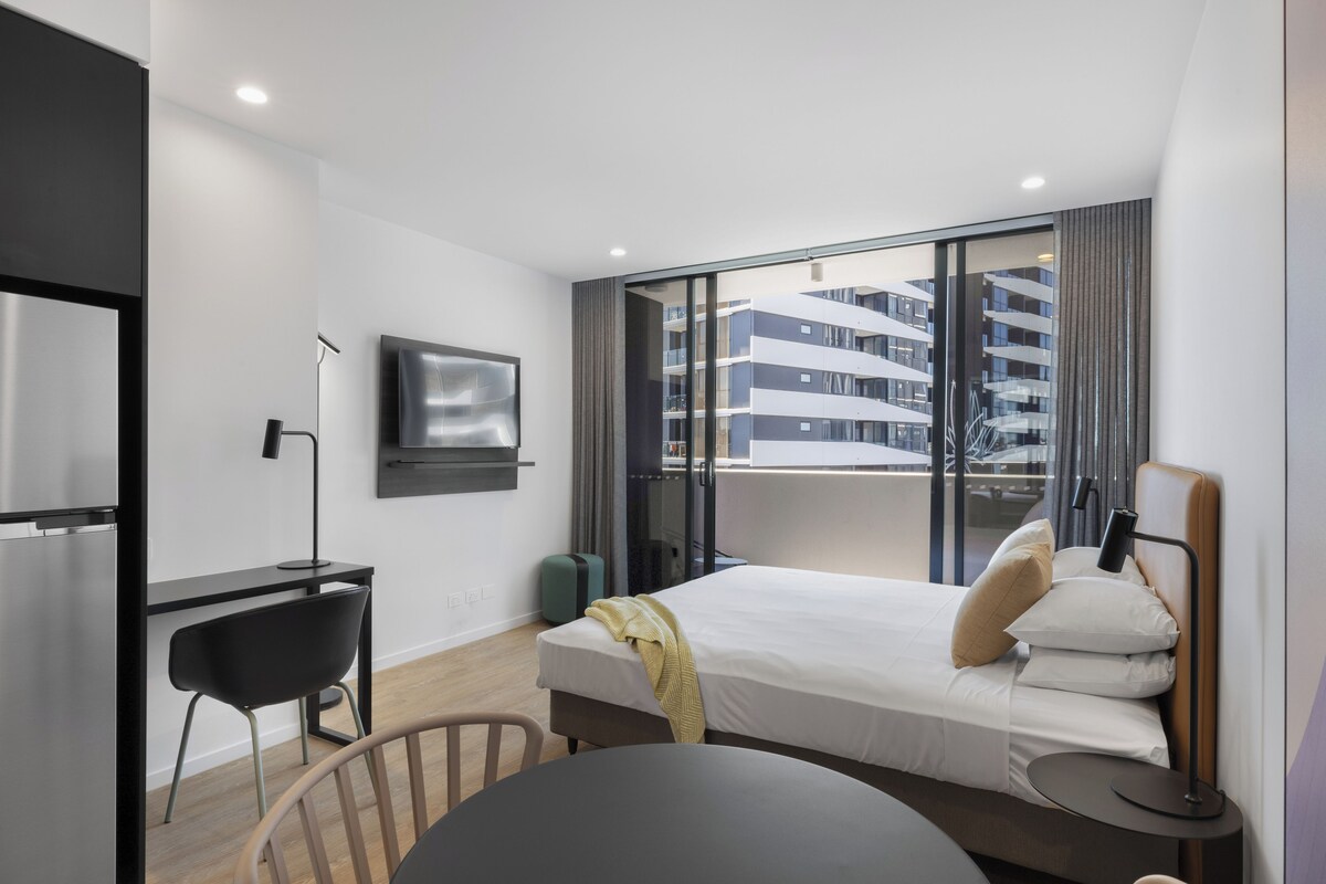 Una habitación de hotel moderna con cama, escritorio, silla y televisor montado en la pared.