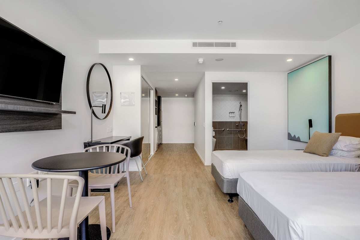 A hotel room with a bed, a desk with chairs, a TV, and a bathroom with a shower.