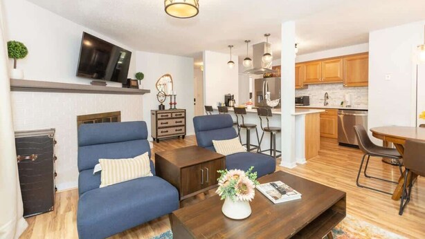 A modern living room with a sofa, coffee table, and TV. There is a kitchen area with wooden cabinets and a dining table. - Cozy Single-Story near Pineville Hospital, games (Charlotte)