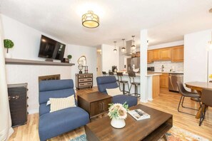 Una sala moderna con un sofá, una mesa de centro y un televisor. Cuenta con una zona de cocina con armarios de madera y una mesa de comedor.