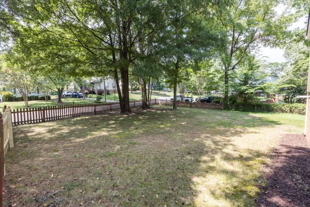 A residential backyard with a wooden fence, trees, and a grassy lawn.