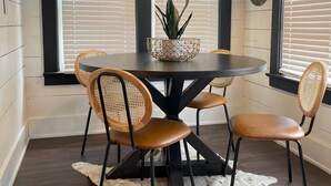 Een eetruimte met een ronde tafel, vier stoelen, een hanglamp en een potplant.