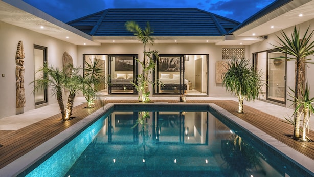 Un área moderna junto a la piscina, con piscina cristalina, cubierta de madera y plantas tropicales.