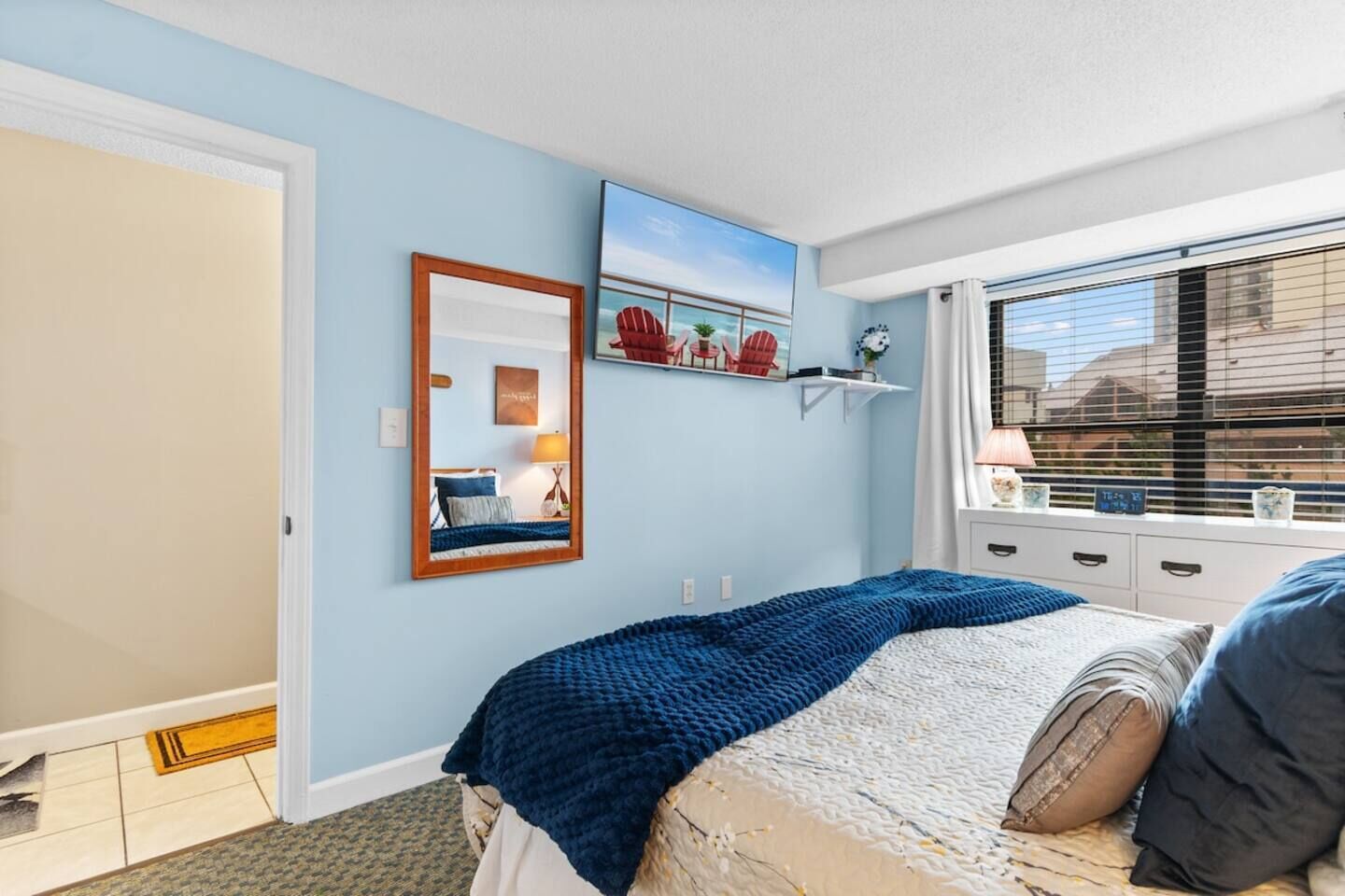 Een slaapkamer met een bed, een spiegel, een raam met zonwering en een wandplank met decoratieve voorwerpen.