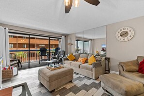 A spacious living area with a sofa set, a coffee table, and a dining table. There is a balcony with chairs and a view of the building's exterior. - Oceanview, Pools, Hot tub, Indoor pool, 2 Beds (Myrtle Beach)