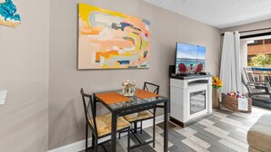 A modern living room with a dining area, a flat-screen TV, and a large abstract painting.