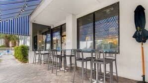 An outdoor seating area with tables and chairs, a covered patio, and a view of the street.