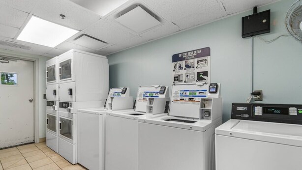 A laundry facility with multiple washing machines and dryers, a control panel, and a sign on the wall.