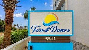 A sign for 'Forest Dunes' with a beach and palm tree in the background.