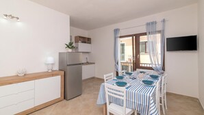 A compact kitchen with a refrigerator, a dining table set for four, and a TV mounted on the wall.