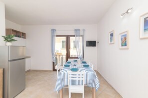 A modern kitchen with a refrigerator, dining table set with blue and white striped tablecloths, and a TV mounted on the wall.