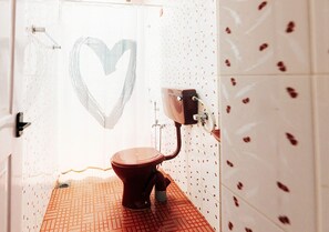 Un baño con una ventana en forma de corazón, un inodoro rojo y azulejos estampados.