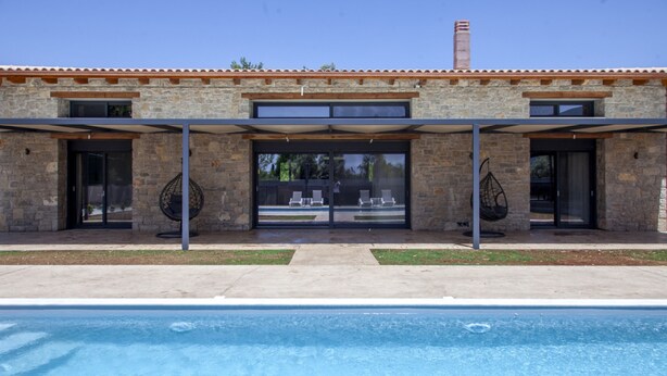 A modern building with a pool, stone facade, and outdoor seating area. - Villa Olia in Agios Petros (Lefkada)