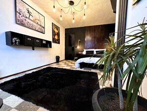 A modern bedroom with a black shag rug, a bed with white and black bedding, a potted plant, and artwork on the walls. - HOMSTY (San Martin Texmelucan)