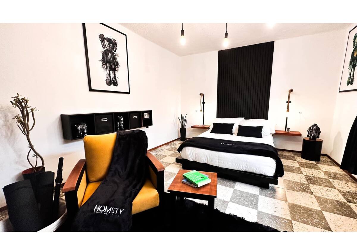 A modern bedroom with a bed, a chair, a small table, and a potted plant.