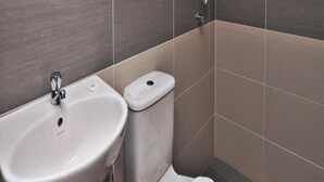 Une salle de bain avec un lavabo, des toilettes et une douche, le tout de couleur blanche.