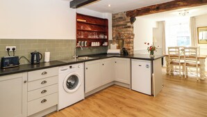 A modern kitchen with a built-in washing machine, a sink, and a wooden dining area. - Kilderkin (Bedale)