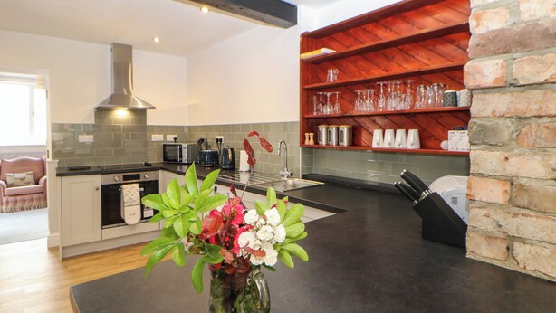 A modern kitchen with a black countertop, a stainless steel range hood, and a brick accent wall. - Kilderkin (Bedale)