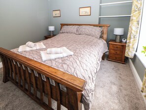 A neatly made bed with a wooden headboard, two bedside tables with lamps, and a small nightstand with a lamp. - Kilderkin (Bedale)