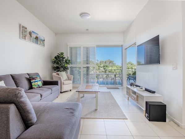 Relax in this stylish living room with a sofa, armchair, and large flat-screen TV. Enjoy the view from the sliding glass door leading to the outdoor balcony.