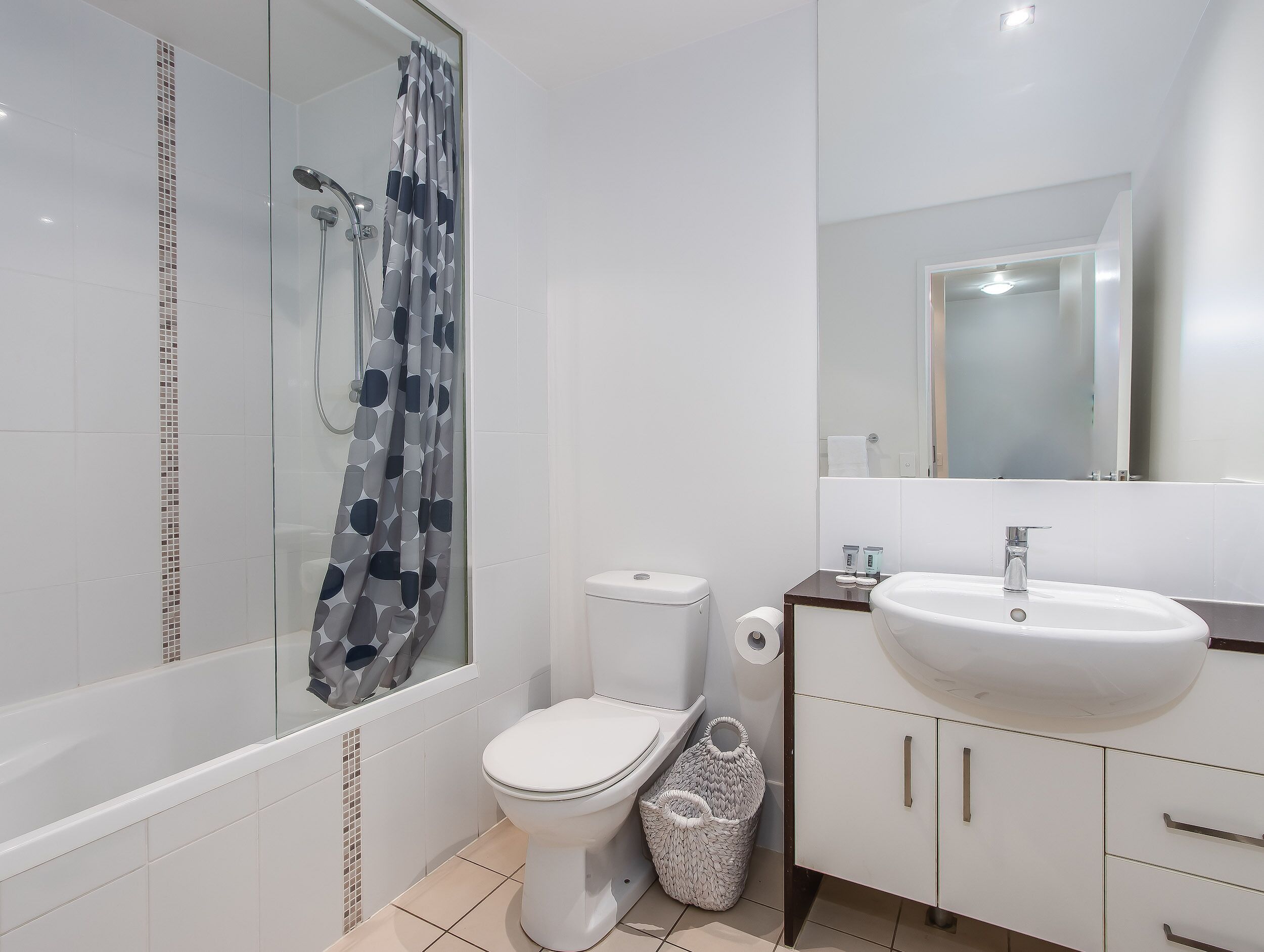 A modern bathroom with a glass shower enclosure, a white toilet, a sink with a mirror, and a tiled floor.