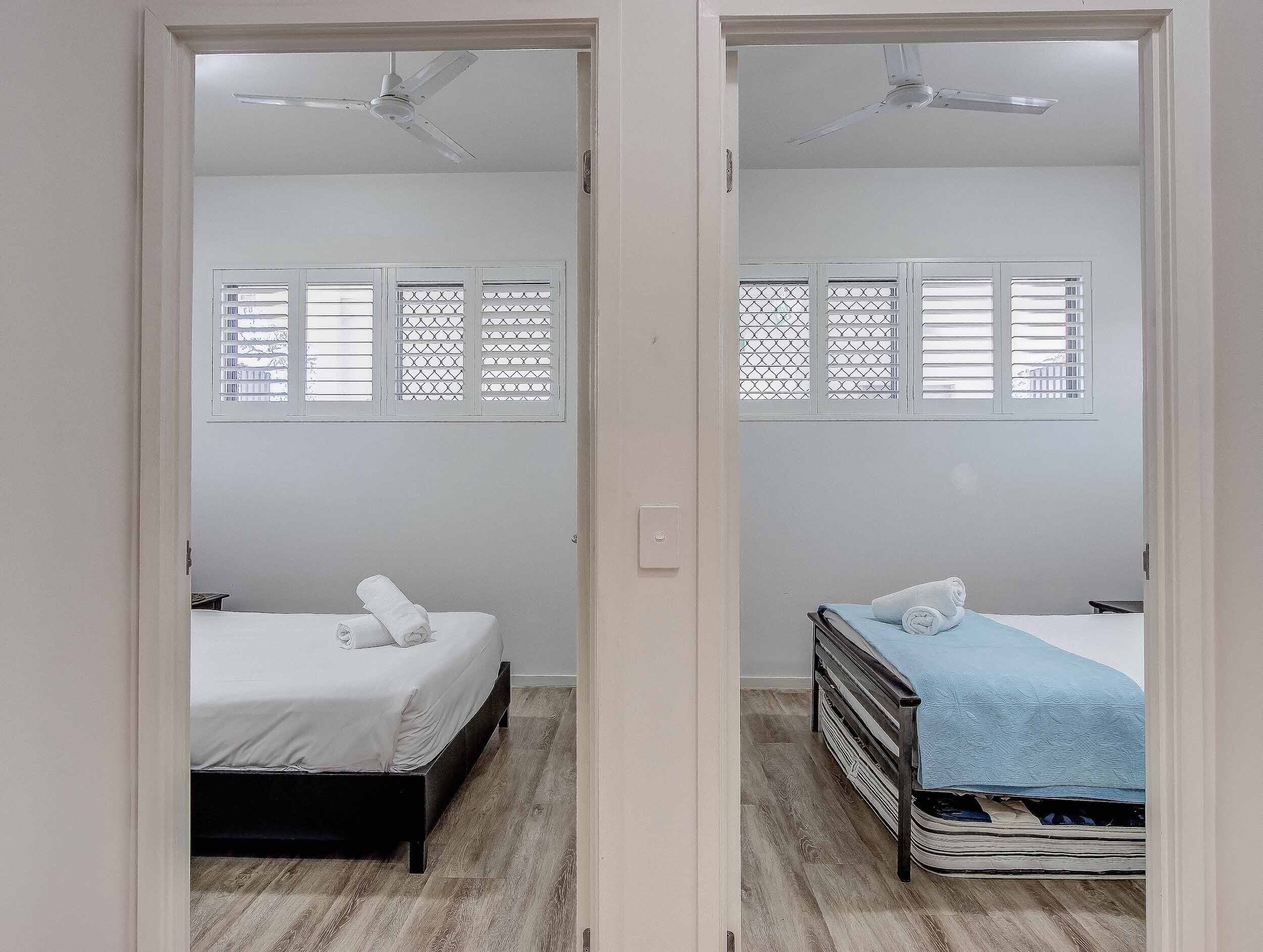 A mirrored room with two beds, a ceiling fan, and a window with a lattice design.