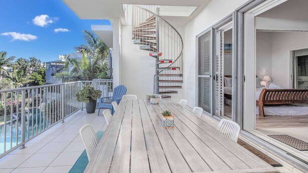 Un balcon spacieux avec une table et des chaises en bois, un escalier en colimaçon et une vue sur les environs.