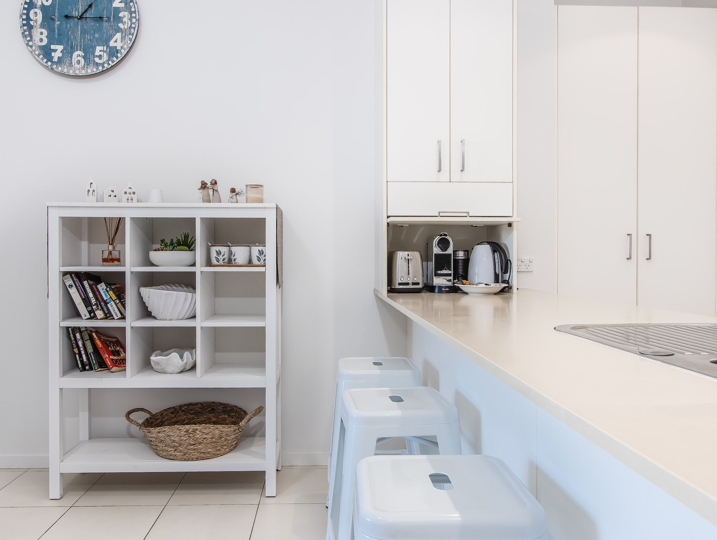 A compact kitchen with white cabinetry, a white countertop, and a clock on the wall.